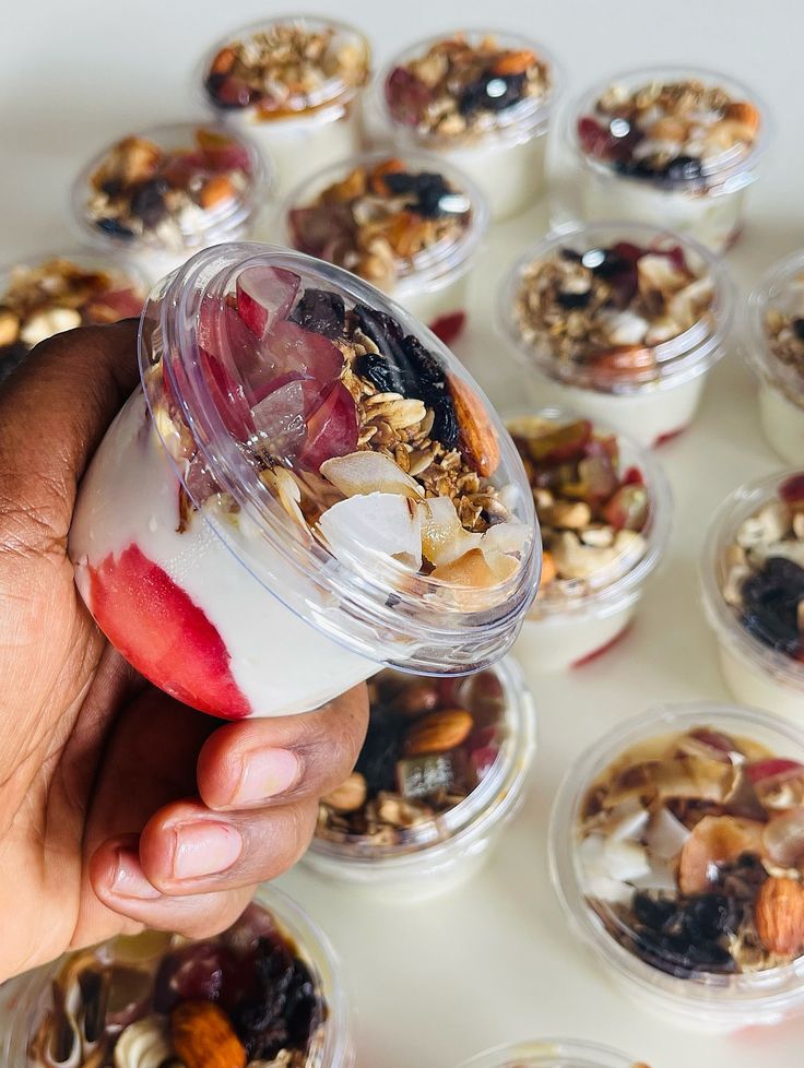 A hand holding a parfait cup topped with granola, almonds, coconut and dried fruit
