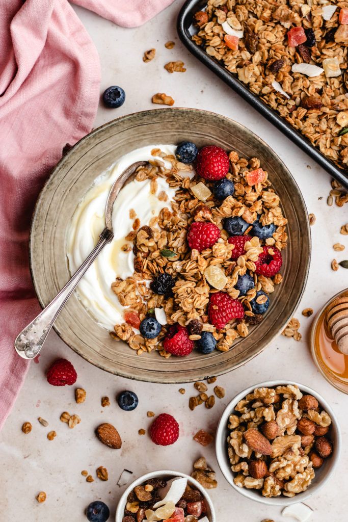 A bowl of yogurt with granola and berries, with nuts and honey beside it